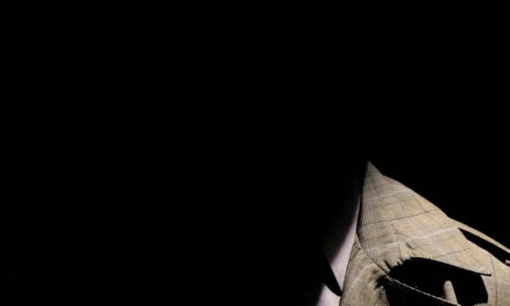 person wearing gray plaid notched lapel suit jacket and gray hat hiding face