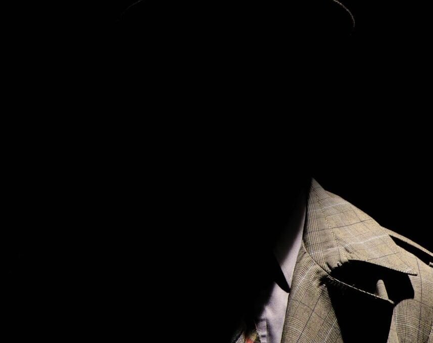 person wearing gray plaid notched lapel suit jacket and gray hat hiding face